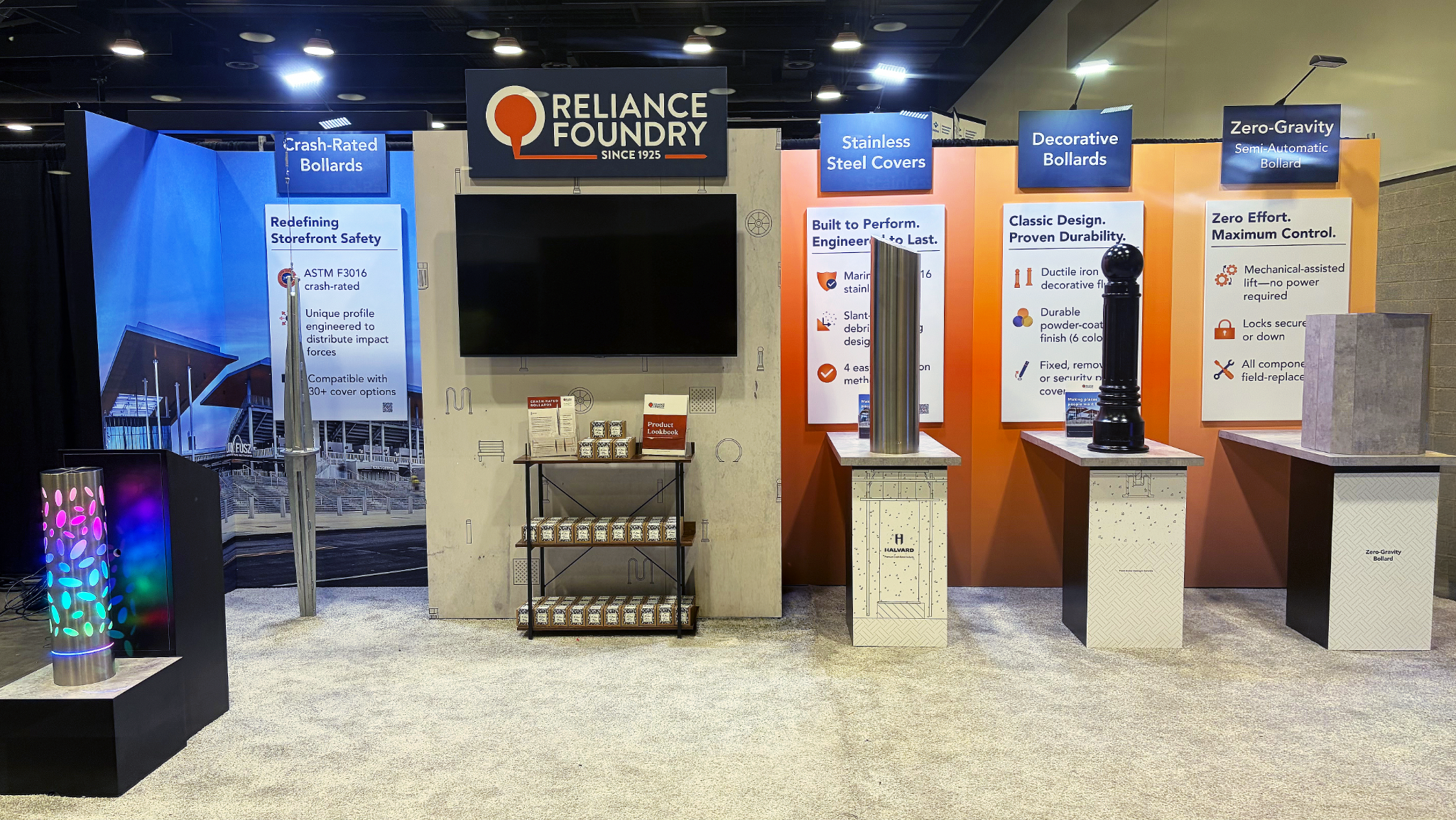 A booth displaying wrap-around graphics, a display screen, merch display shelves, colourful lit up bollard, clean light carpet, and decorative bollards on counters for interactivity.